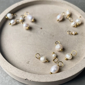 Detailed view of white baroque pearl pendants with gold rings on a stone tray