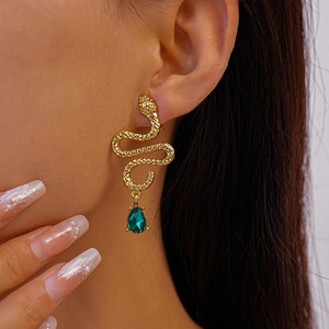Macro detail of gold snake-shaped earrings featuring textured scales and green drop stone