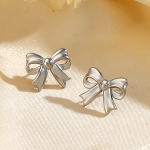 Polished silver stainless steel bow knot stud earrings on beige textured fabric