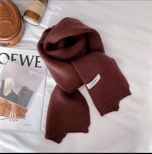 Detail of soft dark brown knitted scarf with woven texture and small brand label on white linen