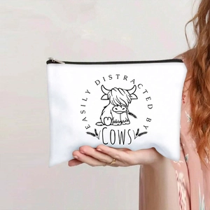 Detail of canvas makeup bag with Highland cow print and black zipper held by hand