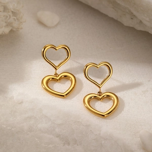 Detailed close-up of double-layered gold heart drop earrings on a white stone background