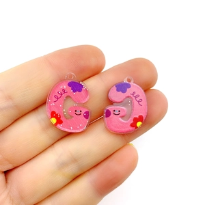 Detail of pink acrylic letter G pendant with cute cartoon smiley and floral patterns