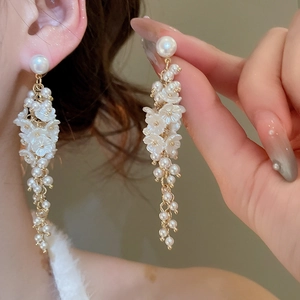 Detail of long floral tassel earrings with white pearls and gold metal finish