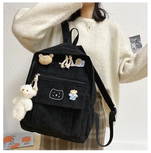 Detalle de mochila de pana negra con pines de dibujos y colgante de osito blanco