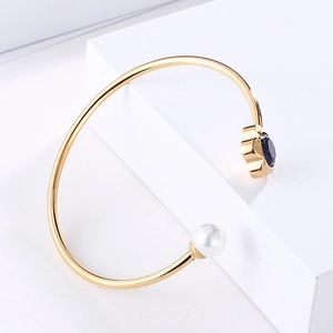 Close-up of gold open bangle with white pearl and navy blue flower gemstone detail