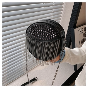 Close-up of black round leather crossbody bag with dark metal studs and fringe chain details