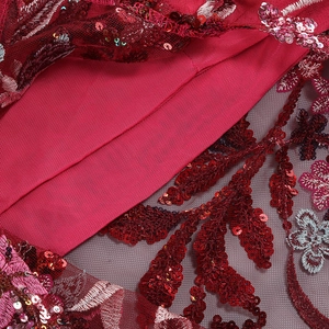 Macro detail of red lace fabric with sequins and floral embroidery on a tulle base