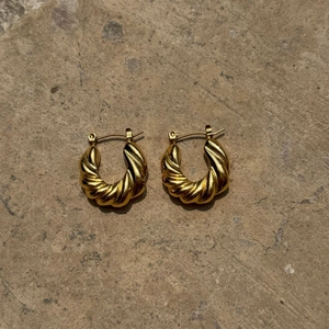 Detail of gold-plated croissant earrings with twisted texture on a textured stone base