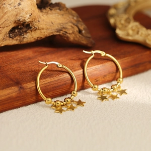 Macro shot of gold hoop earrings with small beads and star charms on a rustic wood background