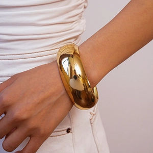 Close-up of minimalist gold-plated wide cuff bracelet with a polished mirror finish