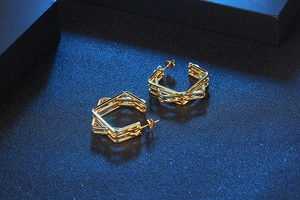 Detailed view of golden multi-layer geometric hoop earrings on a dark textured background