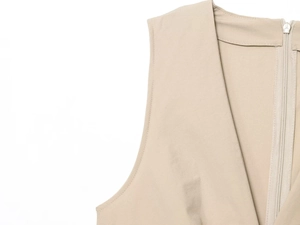 Detailed view of beige V-neck dress featuring back zipper and fine textured pleats