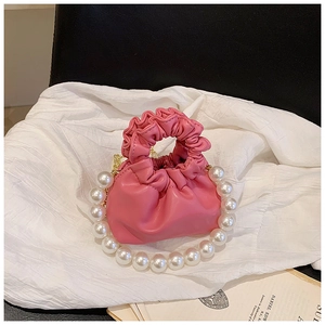 Close-up of a pink pleated bucket bag with a white pearl handle on white fabric