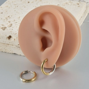 Detail of two-tone stainless steel hoop earrings in gold and silver on a textured stone