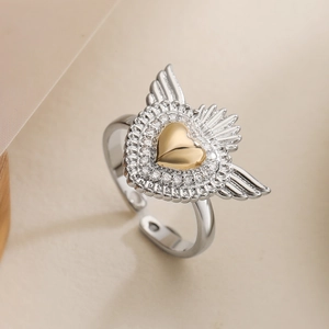 Two-tone silver wings and gold heart open ring with white zircon stones on beige background