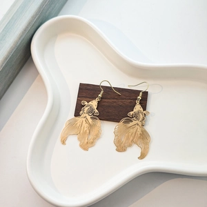 Detailed view of golden hollow-out goldfish earrings on a dark wood display base