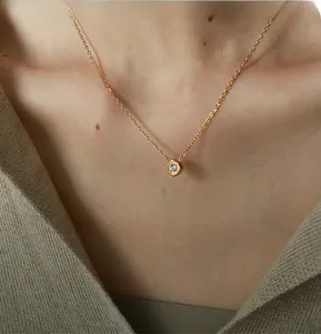 Detail of a minimalist gold geometric necklace with zircon pendant worn by a model