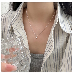Close-up of a delicate silver heart necklace worn by a model in a casual setting