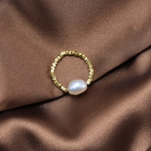 Detailed view of 8.5mm baroque pearl on golden silver ring over brown silk fabric