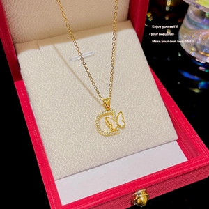 Close-up of 18K gold D-letter pendant with pavé stones and white butterfly on a red box