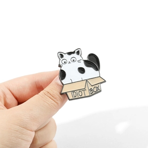 Détail d'un pin's émaillé montrant un chat noir et blanc dans un carton Idiot Box