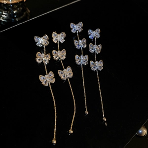 Détail de boucles d'oreilles nœuds dorés avec pompons en cristal et pierres de zircon