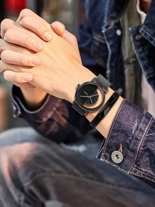 Close-up of TOMI watch with grey leather strap and black bracelet on a wrist