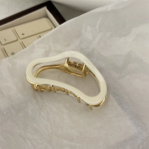 Detail view of the elegant wavy gold-tone hair claw clip with cream enamel finish