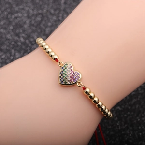 Bracelet à perles dorées avec pendentif cœur en zircon coloré porté au poignet