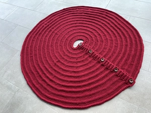 Close-up of deep red knitted Christmas tree skirt with five buttons and wool texture