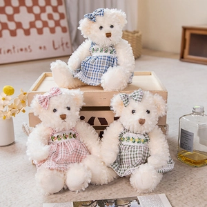 Three plush teddy bears in plaid dresses with floral embroidery in a warm home setting