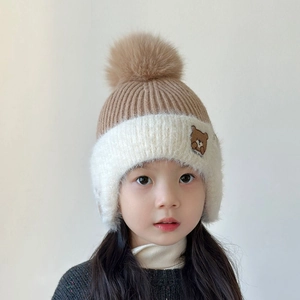 Detailed knit texture of a brown and white winter hat with bear embroidery and pom pom