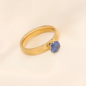 Bague élégante en acier doré avec une pierre bleue ronde sur un fond de soie