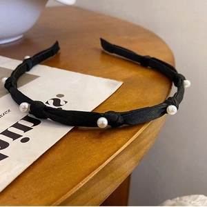 Elegant black fabric headband with faux pearl accents on a stylish magazine