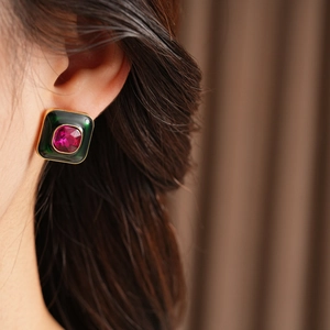 Close-up of vintage gold earring with green enamel and rose red gemstone on a model