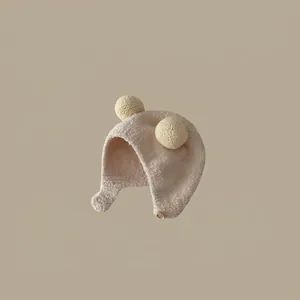 Detail showing beige fleece kids thermal hat with cute yellow pompom ears and earflaps