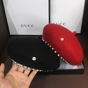 Detail of wool beret hat with white pearls and gold metal initial charm in black and red