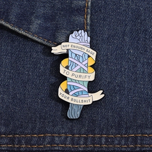 Detail of enamel sage pin with cheeky slogan on dark denim fabric background