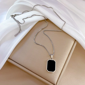 Macro shot of silver box chain and rectangular pendant with black inlay on silk cloth