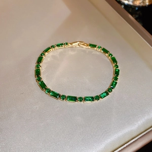 Detailed view of a gold-plated tennis bracelet with emerald green crystals in a gift box