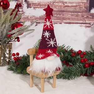 Detail of Christmas gnome sitting on a wooden chair with cozy festive holiday scenery