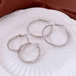 Minimalistische silberne Creolen in zwei Größen auf einem dekorativen weißen Porzellanteller