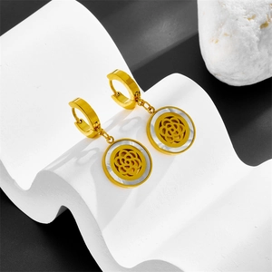 Gold hoop earrings with white shell flower pendant on elegant stone backdrop
