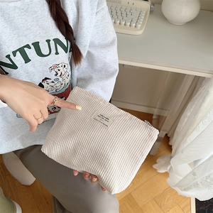 Detail of beige corduroy pouch with a woven patch held in a bright lifestyle setting
