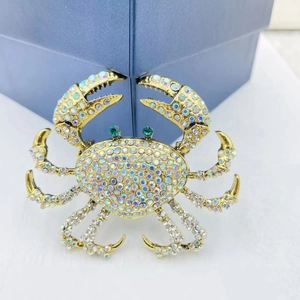Exaggerated gold crab brooch with colorful rhinestones and green gemstone eyes on gift box