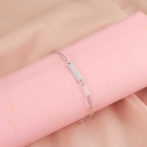 Detailed macro view of a silver stainless steel paperclip chain bracelet with a blank ID tag