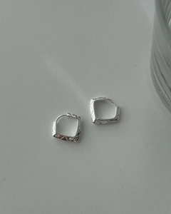 Macro shot of silver geometric square earrings featuring refined rhombic texture details