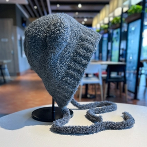 Dettaglio cappello in maglia grigia con orecchie da orso e lunghi lacci intrecciati