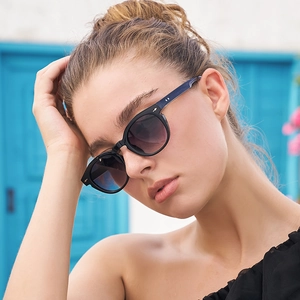 Fashionable black oval sunglasses with purple gradient lenses worn by model on blue background